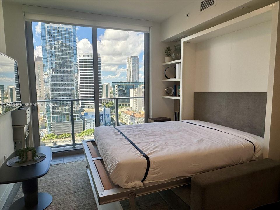 Floor-to-ceiling windows, built-in shelving, retractable bed system, and private balcony with metropolitan backdrop