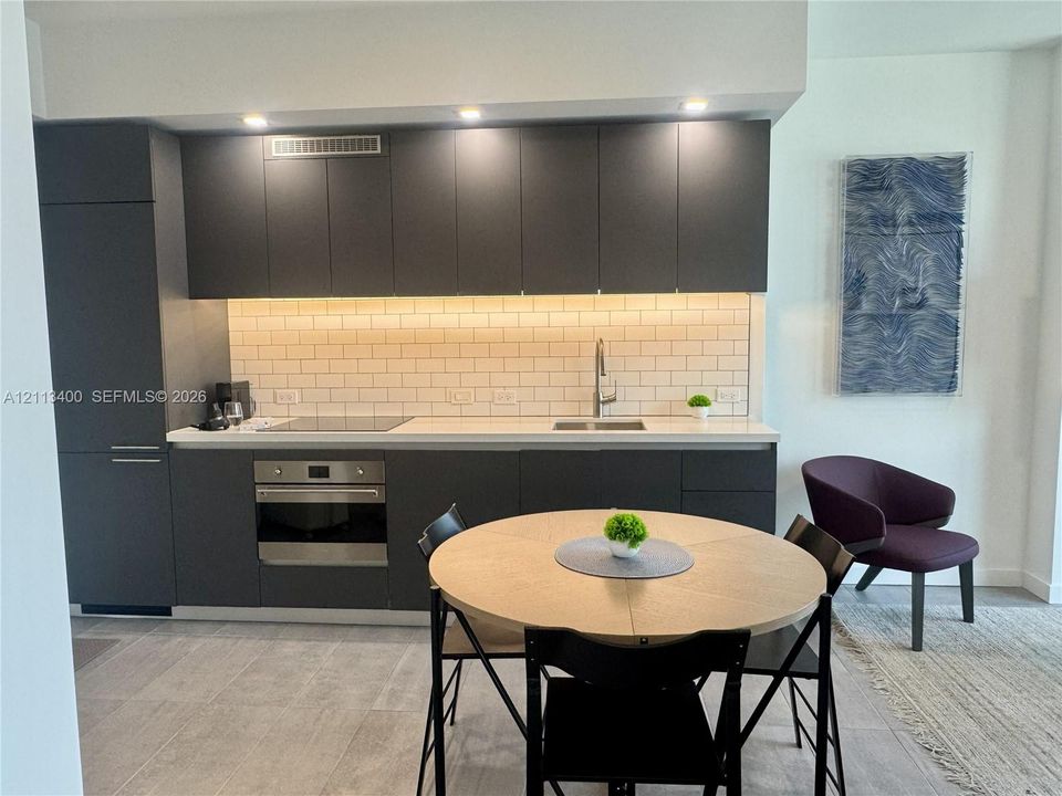 Kitchen featuring matte charcoal flat-panel cabinetry, light-toned countertop, subway tile backsplash, built-in stainless steel oven, and recessed lighting