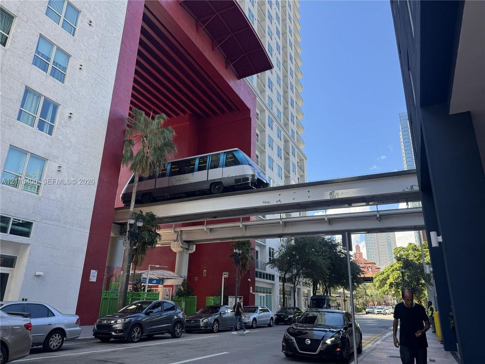 Exterior urban streetscape featuring multi-story high-rise structures, a concrete transit infrastructure rail system, and paved roadway