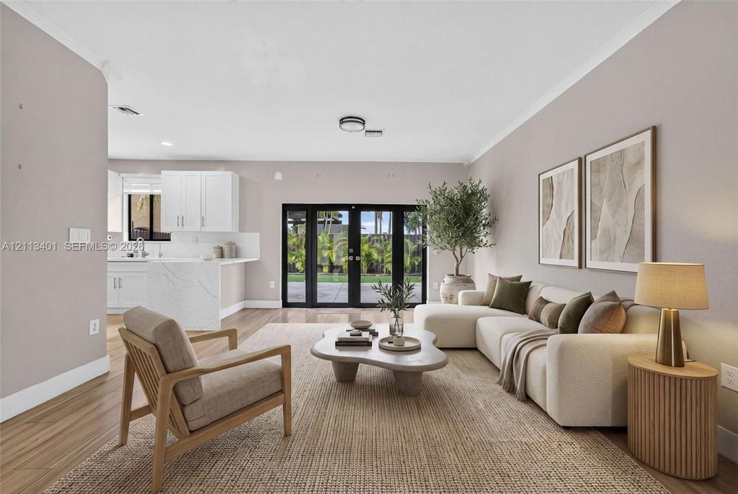 Open-concept living space featuring wood-finish flooring, white kitchen cabinetry, a waterfall-edge stone island, and black-framed French doors