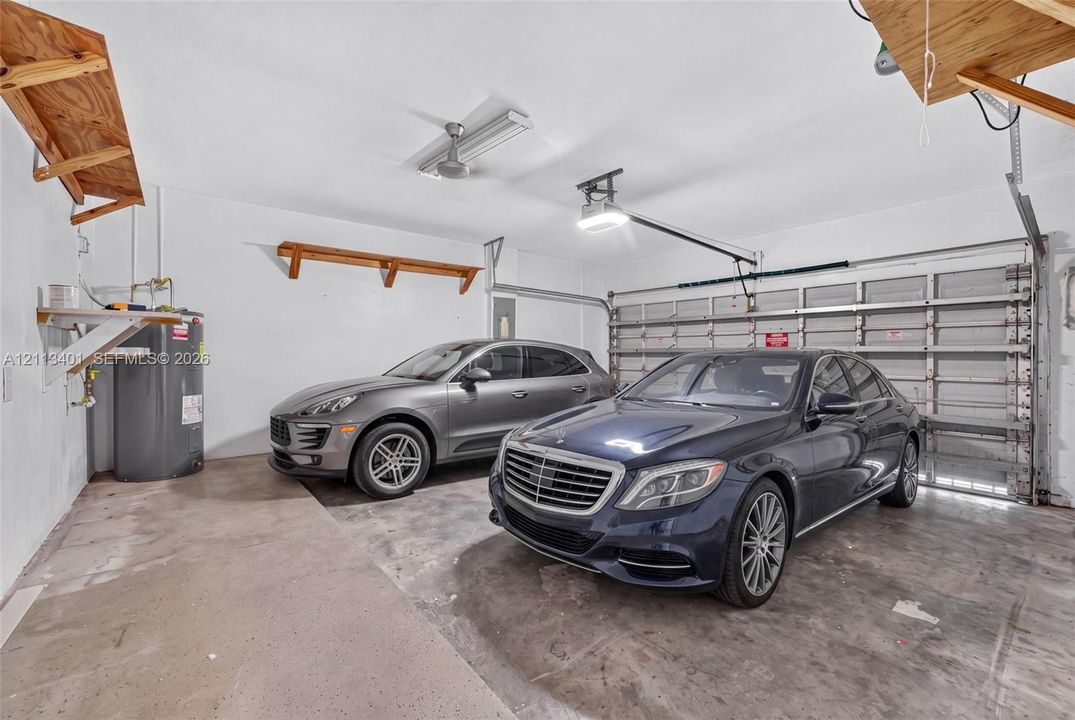 Two-car garage featuring a concrete floor, sectional overhead door, built-in wooden wall shelving, and a dedicated water heater