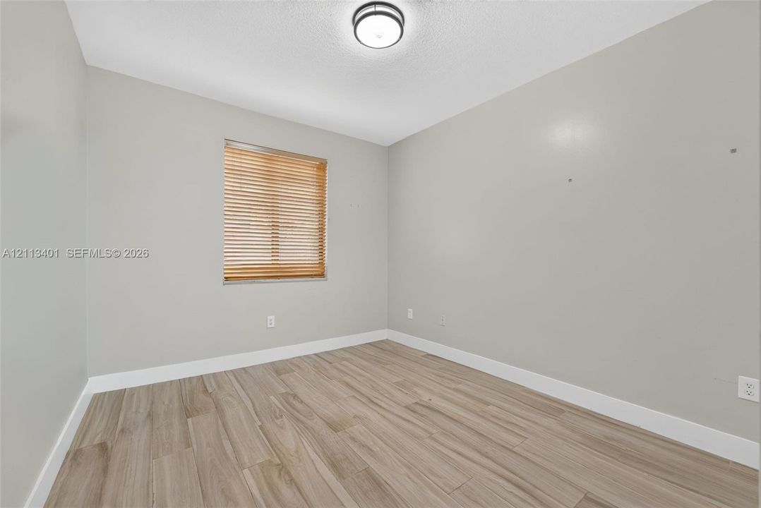 Room featuring neutral-toned walls, wood-finish flooring, a single window with wood-finish blinds, and a circular flush-mount ceiling light fixture
