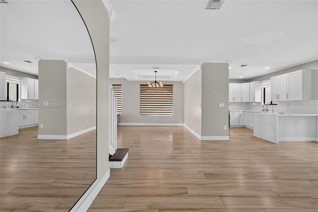 Open-concept interior featuring wood-finish tile flooring, white cabinetry with stone-finish waterfall countertops, recessed lighting, and a modern tiered tray ceiling