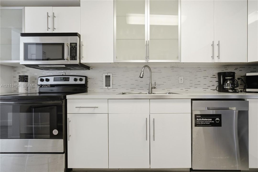White cabinetry featuring glass-panel upper doors, stainless steel appliances, a multi-tonal linear tile backsplash, and a stainless steel gooseneck faucet
