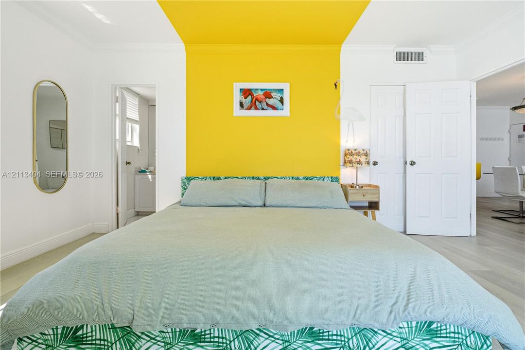 Room featuring wood-finish flooring, a wall-to-ceiling yellow accent, crown molding, and a tall oval wall-mounted mirror