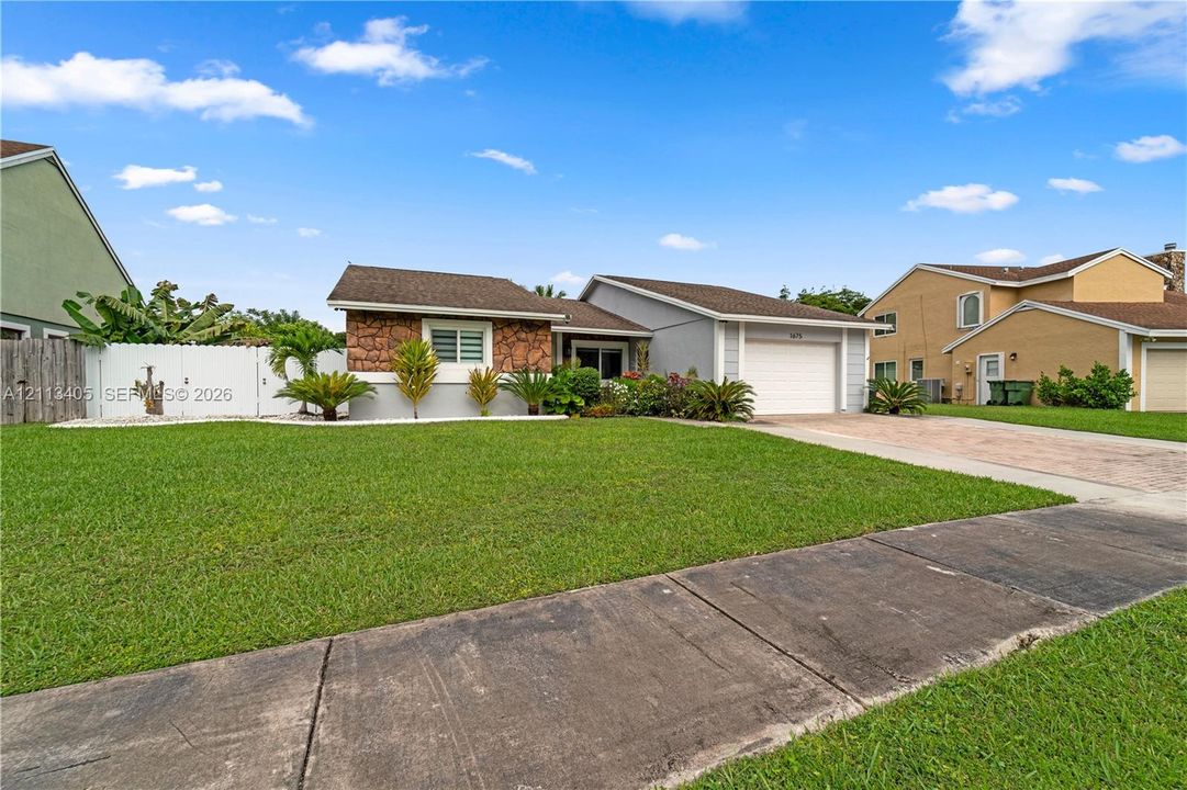 Single-story exterior featuring a stone-veneer facade, attached garage, concrete driveway, and white privacy fencing