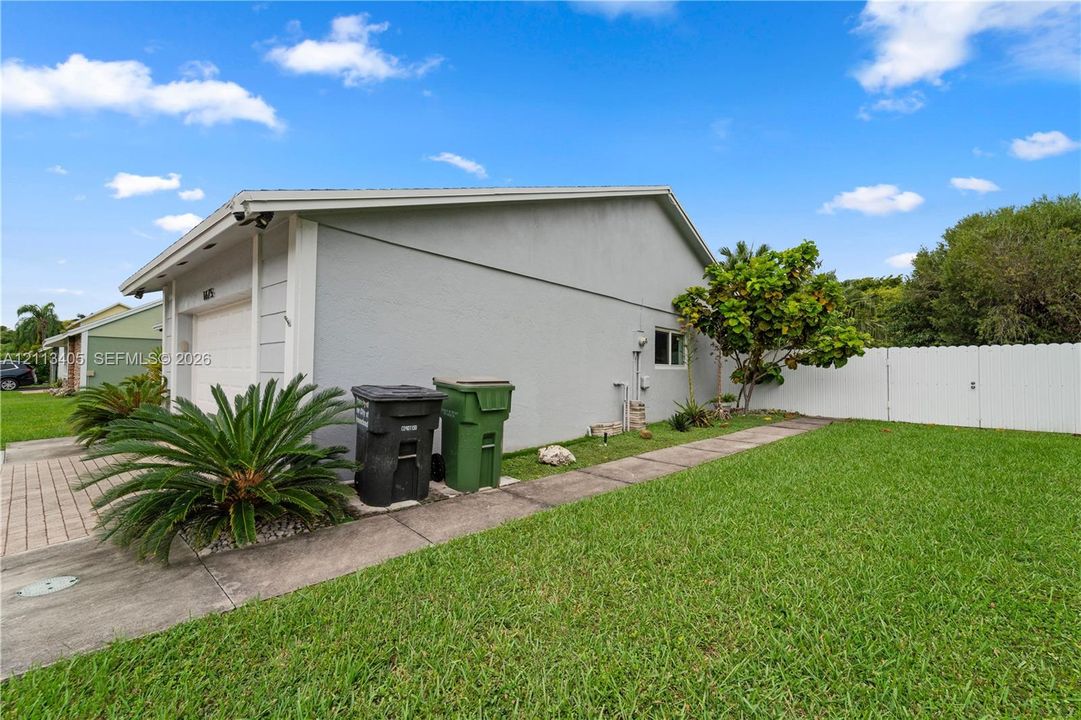 Stucco exterior featuring a paved walkway, attached garage, and white vinyl perimeter fencing