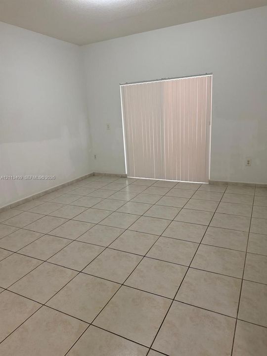 Neutral-toned ceramic tile flooring and sliding glass doors featuring vertical blinds