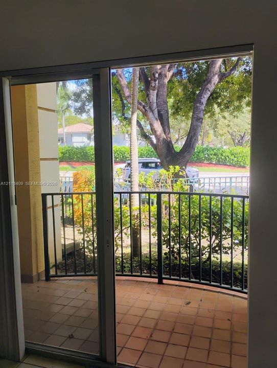 Covered balcony with terracotta tile flooring, metal railing, and sliding glass entry