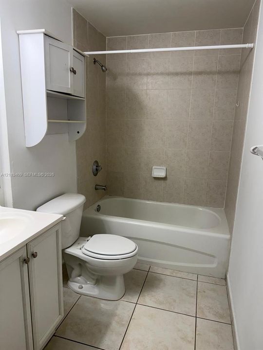Bathroom featuring a tub-shower combination with tile surround, white cabinetry, a vanity with an integrated sink, and tile flooring