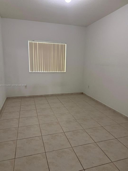 Neutral-toned ceramic tile flooring, clean white walls, and a recessed window featuring vertical blinds