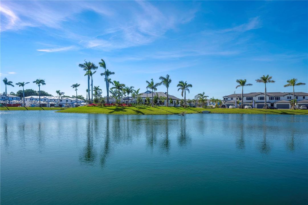 Waterfront property featuring a serene lake, manicured landscaping, and mature palm trees
