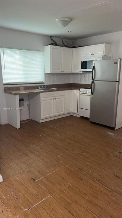 Kitchen featuring white shaker-style cabinetry, wood-finish flooring, stone-finish countertops, stainless steel refrigerator, and integrated microwave