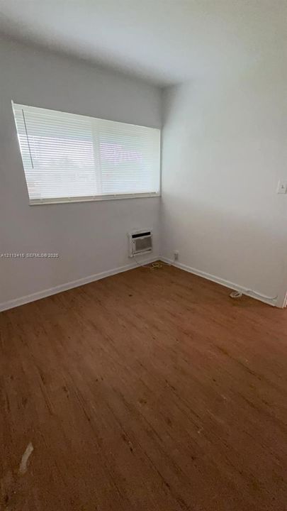 Interior space featuring wood-finish flooring, a wall-mounted air conditioning unit, and a window with horizontal blinds
