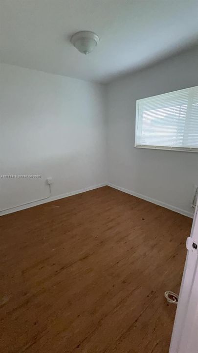 Wood-finish flooring, neutral walls, large window with horizontal blinds, and a semi-flush mount ceiling light