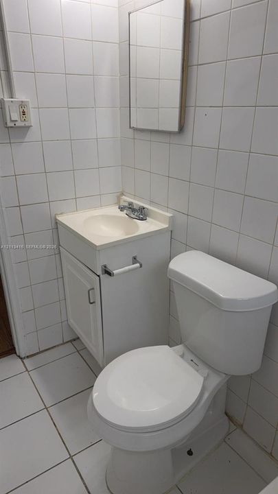 Compact bathroom featuring white tiled walls, square floor tiling, a vanity with an integrated basin, and a wall-mounted mirror