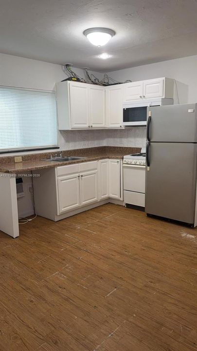 Kitchen featuring white cabinetry, wood-finish flooring, stone-surfaced countertops, and a double-basin stainless steel sink