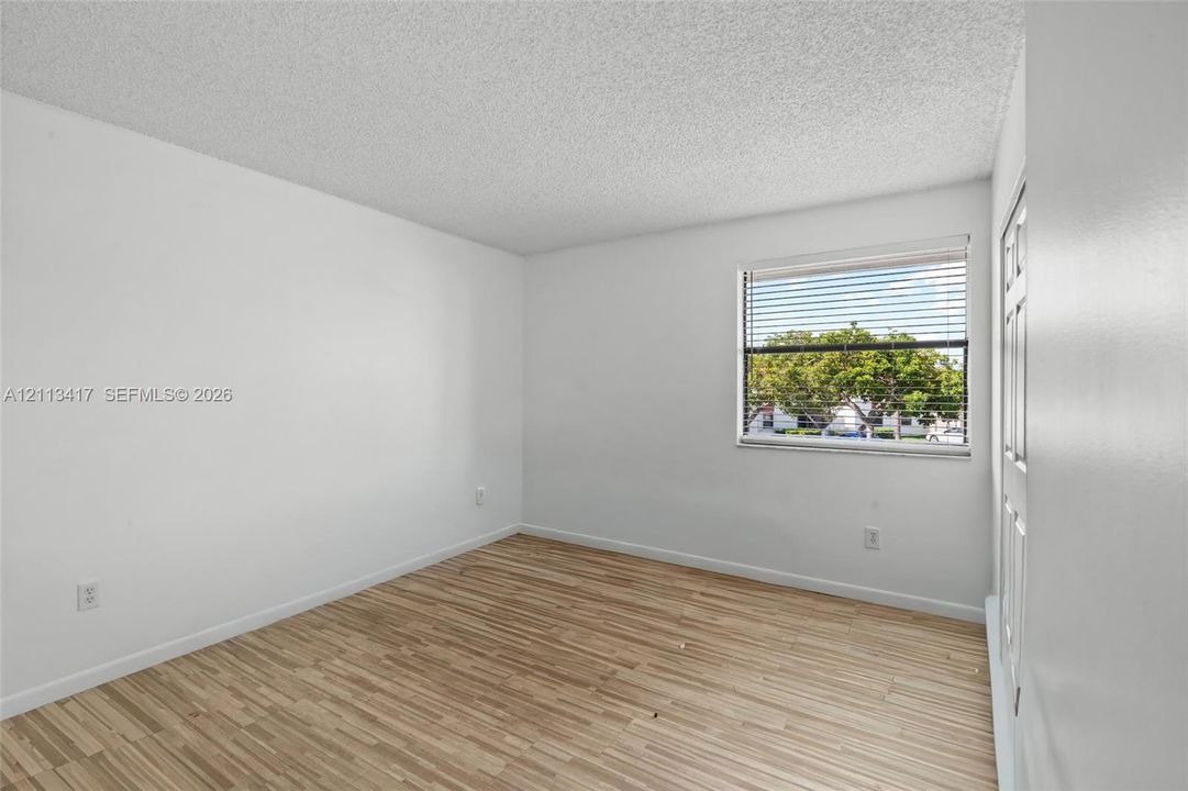 Neutral interior room featuring wood-finish flooring, white walls, and a window with horizontal blinds