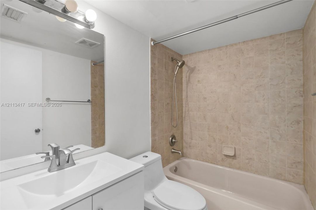 Bathroom featuring a white vanity with integrated basin, polished chrome faucet, large wall-mounted mirror, and tub-shower combination with ceramic tile surround