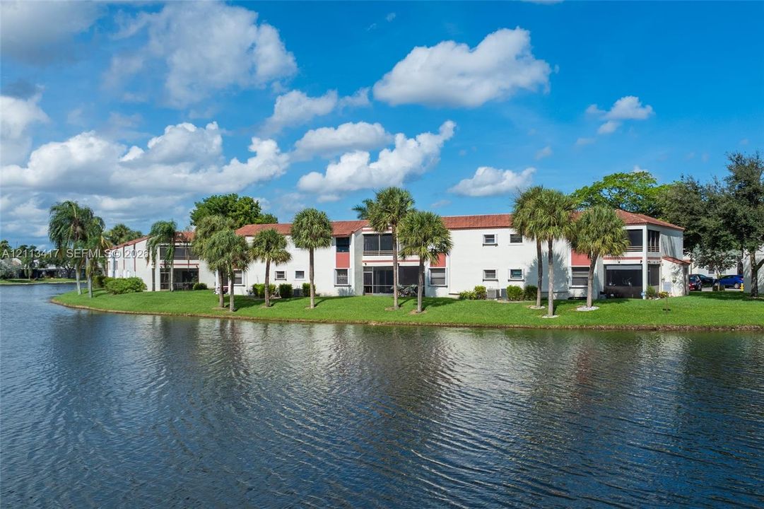 Multi-story exterior featuring a clay tile roof, screened-in balconies, and water frontage with manicured landscaping and mature palm trees