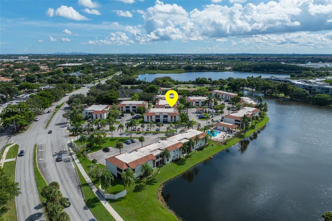 Aerial view featuring multi-story residential buildings with clay tile roofing, manicured green space, a swimming pool, and water frontage