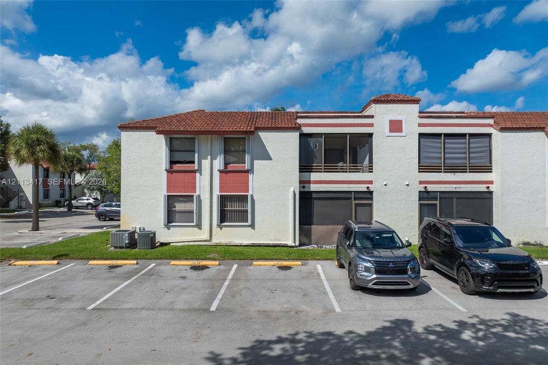 Stucco exterior featuring red tile roofing, accented trim, screened-in balconies, and dedicated surface parking