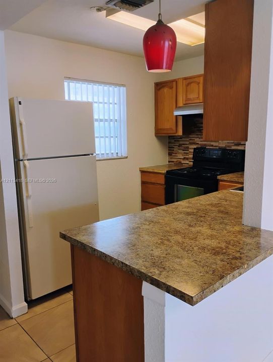 Kitchen featuring wood cabinetry, stone-finish countertops, tile backsplash, and a ceramic-tile floor