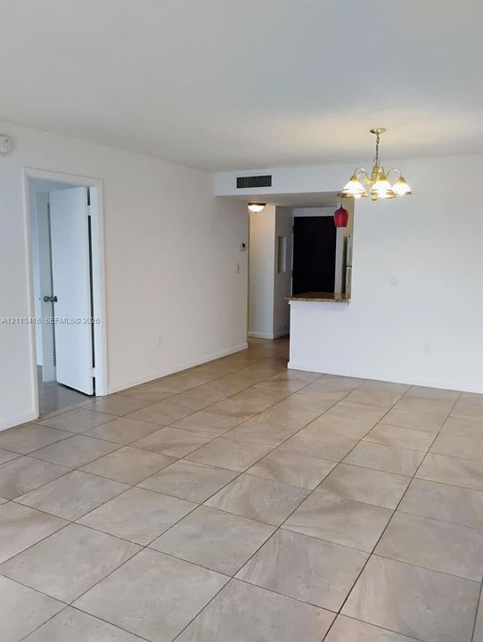 Neutral tile flooring throughout, multi-arm metal chandelier, and pass-through breakfast bar featuring a stone countertop