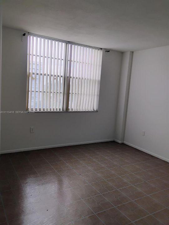 Neutral-toned interior space featuring large window with vertical blinds and ceramic tile flooring