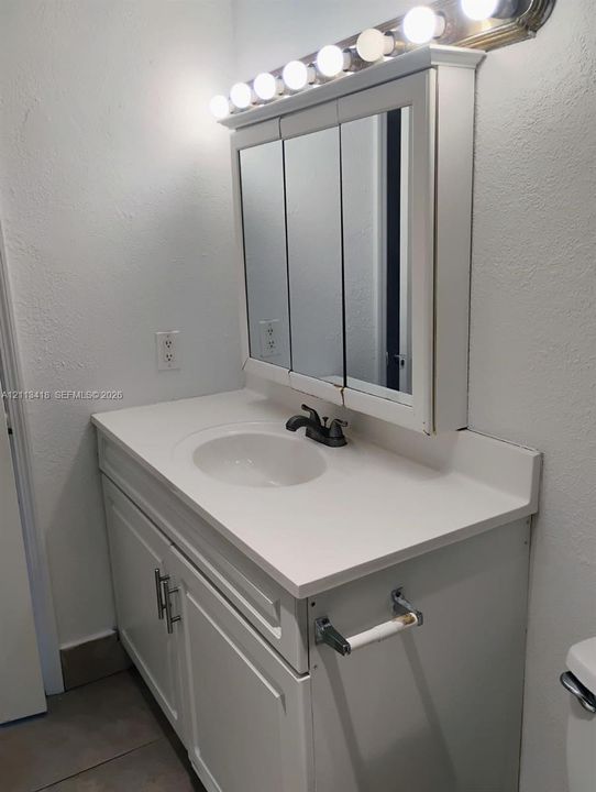 Vanity featuring a white cabinet with brushed nickel hardware, an integrated sink with a dual-handle faucet, a triple-panel mirrored medicine cabinet, and a multi-bulb vanity light fixture