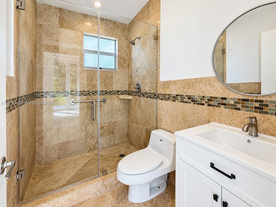 Walk-in shower with a glass enclosure, wall-mounted shower head, and stone-tile surround featuring a decorative mosaic border
