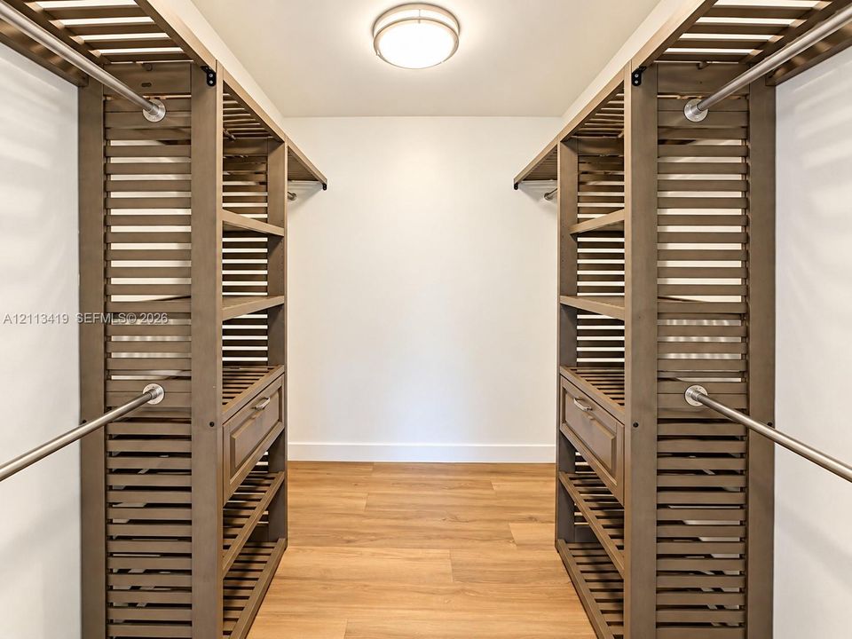 Primary walk-in storage featuring custom wood-slat built-in shelving, integrated drawers, brushed-metal hanging rods, and wood-finish flooring