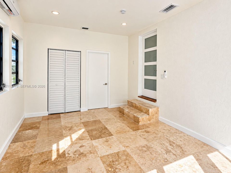Large-format stone flooring, multi-panel glass insert door with a matching stone entry step, louvered bi-fold closet, and recessed lighting