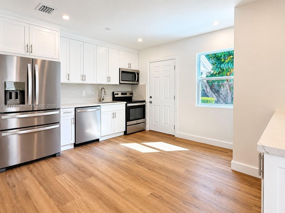 Kitchen featuring white shaker-style cabinetry, stainless steel appliances, stone-finish countertops, and wood-finish flooring