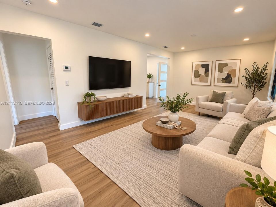 Virtually staged living area featuring wood-finish flooring, recessed lighting, and a wall-mounted floating media console with a slatted wood texture