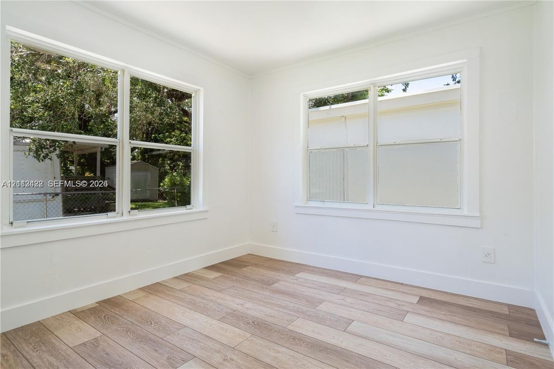 Neutral interior featuring wood-finish flooring, white walls, and large windows with paneled trim