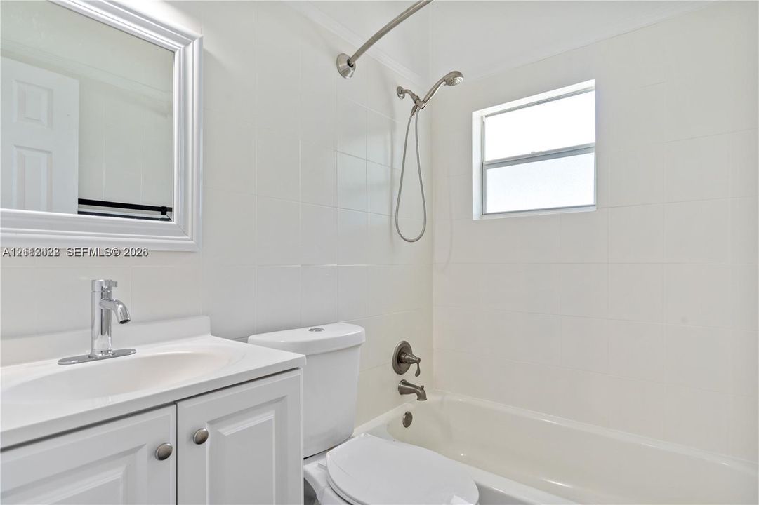 Bathroom featuring white wall tiling, a vanity with a white countertop and chrome faucet, a wall-mounted mirror, and a shower-tub combination with metal fixtures