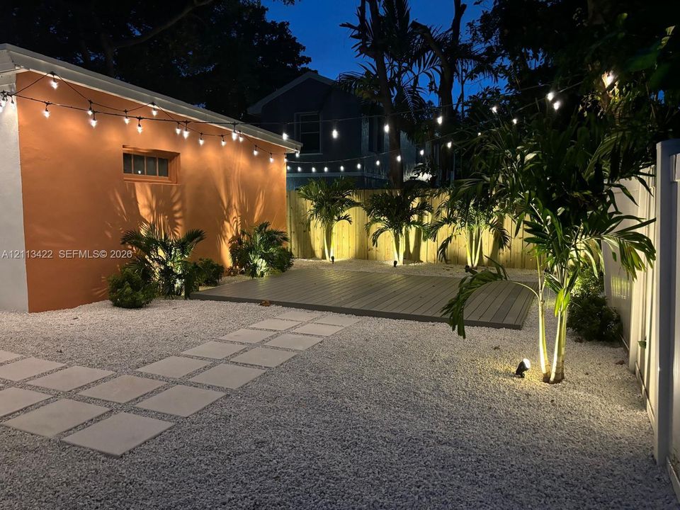 Rear yard featuring a gray composite deck, crushed stone ground cover, concrete paver path, perimeter privacy fencing, and mature palms