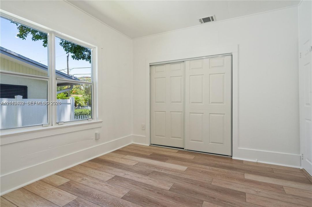 Wood-finish flooring, sliding closet doors with six-panel detail, and large windows providing natural light