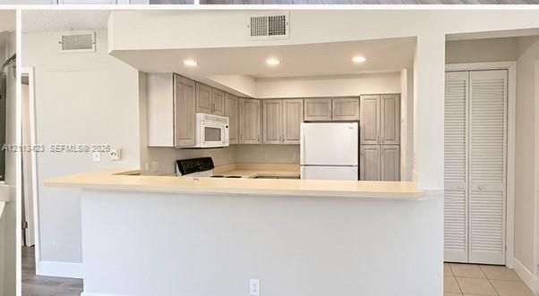 Kitchen featuring light-toned cabinetry, solid surface countertop, recessed lighting, and white appliances