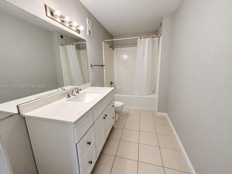 Bathroom featuring a white vanity with drawers, a light-toned countertop, a full-width wall mirror, and a tile-surround shower and tub combination with ceramic floor tile