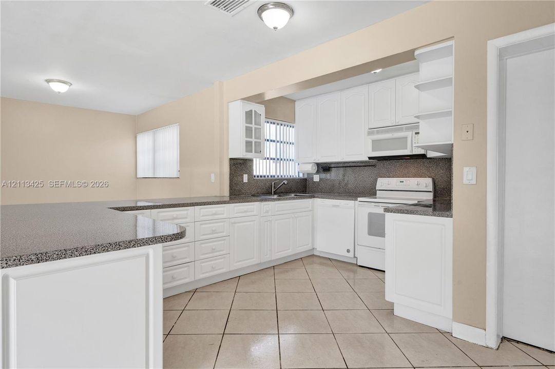 Kitchen featuring white cabinetry, stone-finish countertops, tile flooring, and integrated white appliances