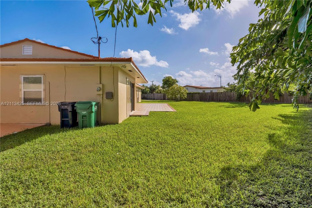Expansive backyard featuring a grass lawn, tiled patio, and perimeter wood fencing