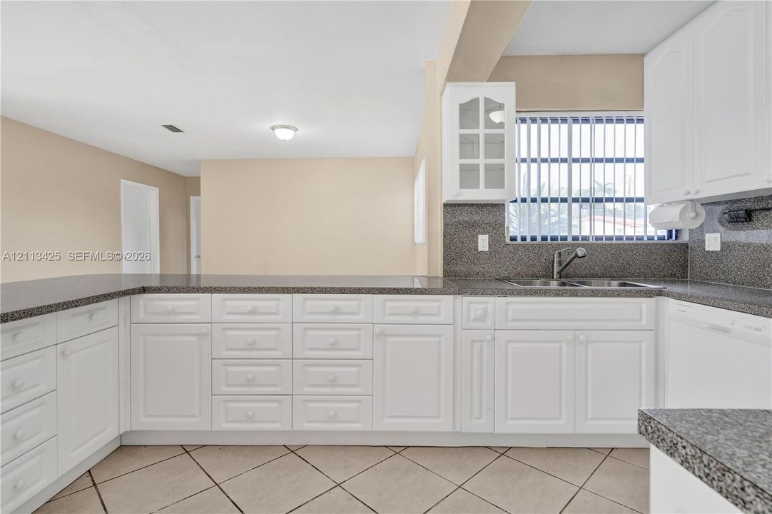 Kitchen featuring white cabinetry with glass-front uppers, speckled stone-finish countertops, stainless steel dual-basin sink, and tile flooring laid on a diagonal