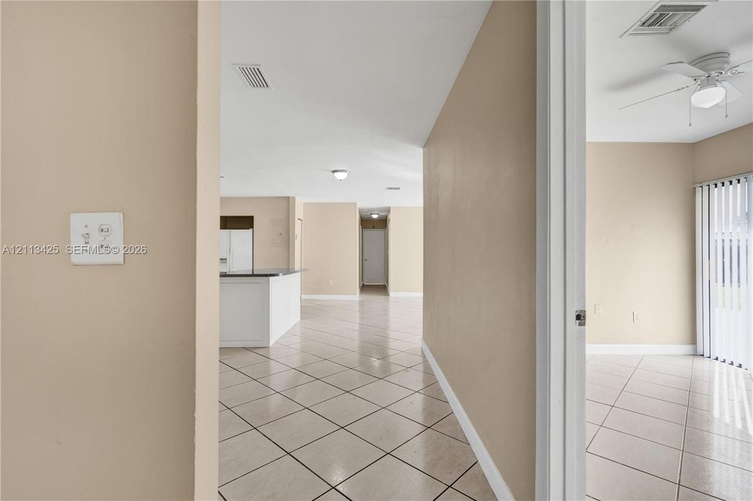 Interior featuring neutral wall paint, tile flooring throughout, a kitchen island with stone-surface countertop, and a ceiling fan with integrated lighting