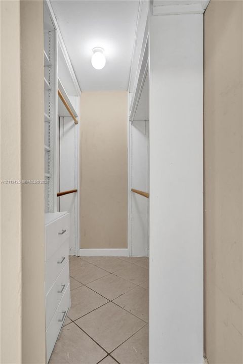 Walk-in closet featuring ceramic tile flooring, built-in drawer storage, white shelving units, and two wood-finish garment rods