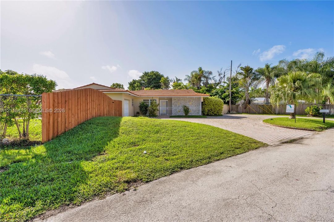 Single-story residence featuring a stone-veneer facade, expansive front lawn, wood privacy fencing, and a paved driveway