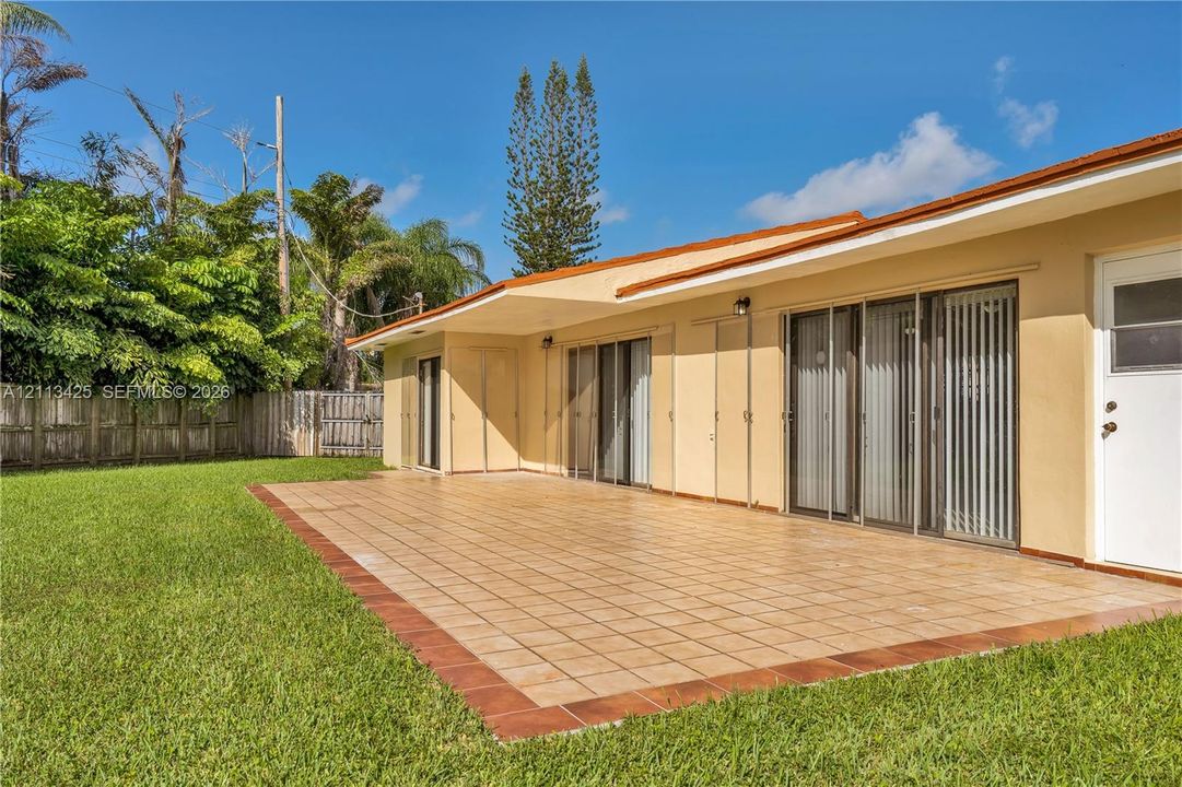Expansive exterior patio featuring ceramic tile flooring, sliding glass doors, and a wood privacy fence