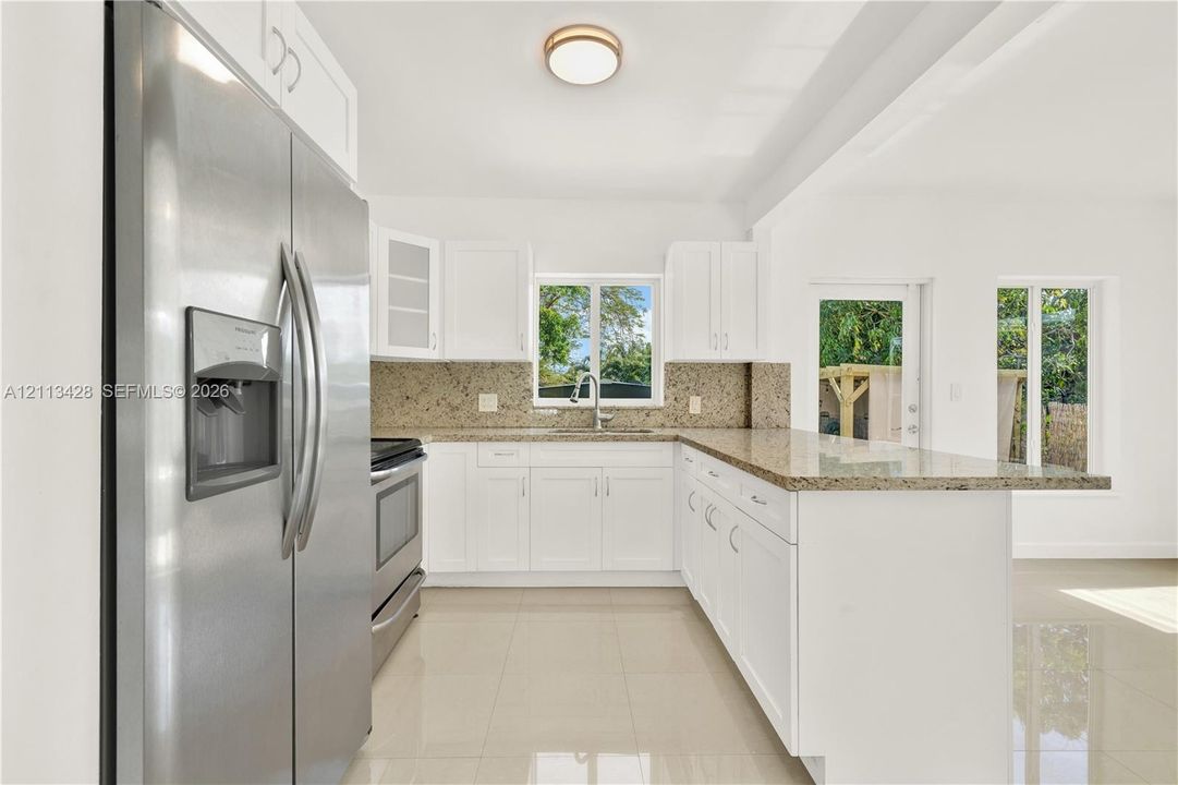 Kitchen featuring white cabinetry, stone-finish countertops, stainless steel appliances, tile flooring, and a peninsula with breakfast bar seating