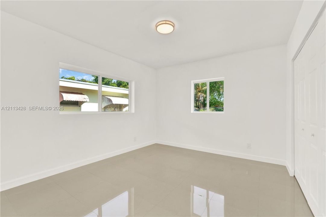 Neutral-toned tile flooring, dual windows, minimalist ceiling-mounted light fixture, and floor-to-ceiling closet with paneled doors